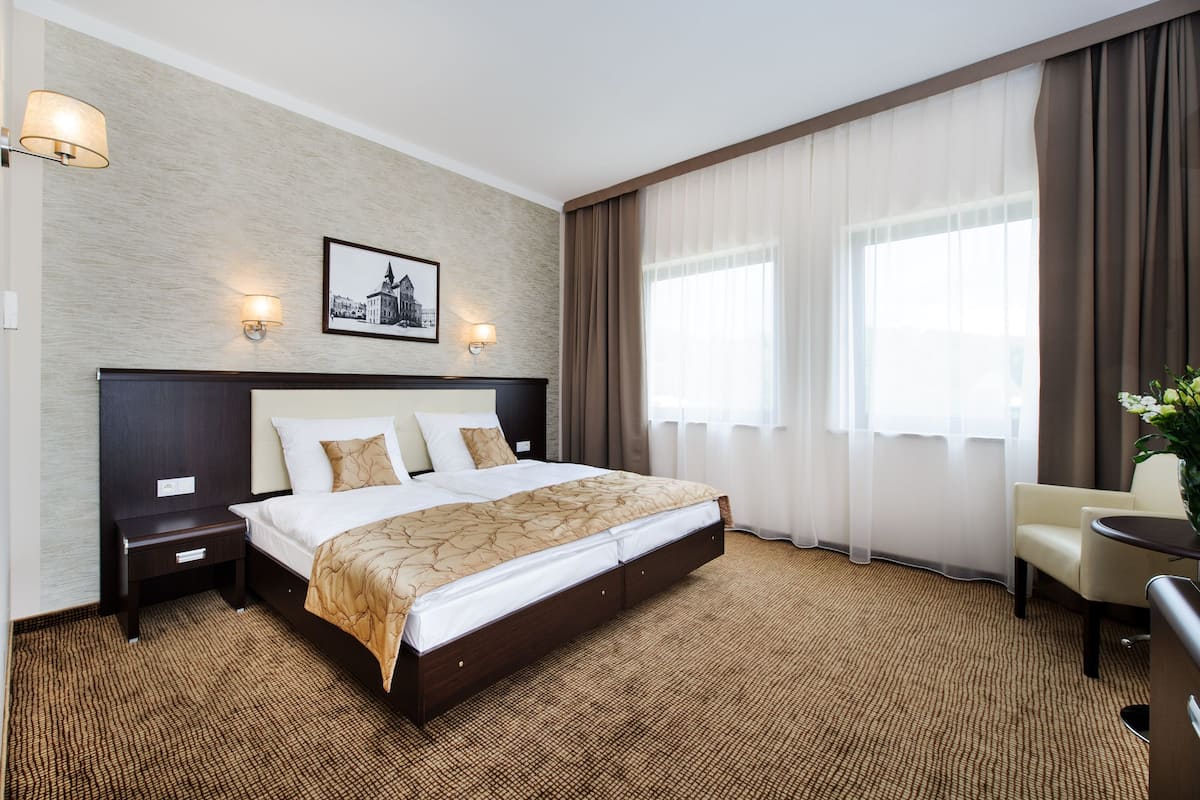 Ett hotellrum med en stor säng, två sängbord, en stol, ett litet bord och en tavla på väggen.