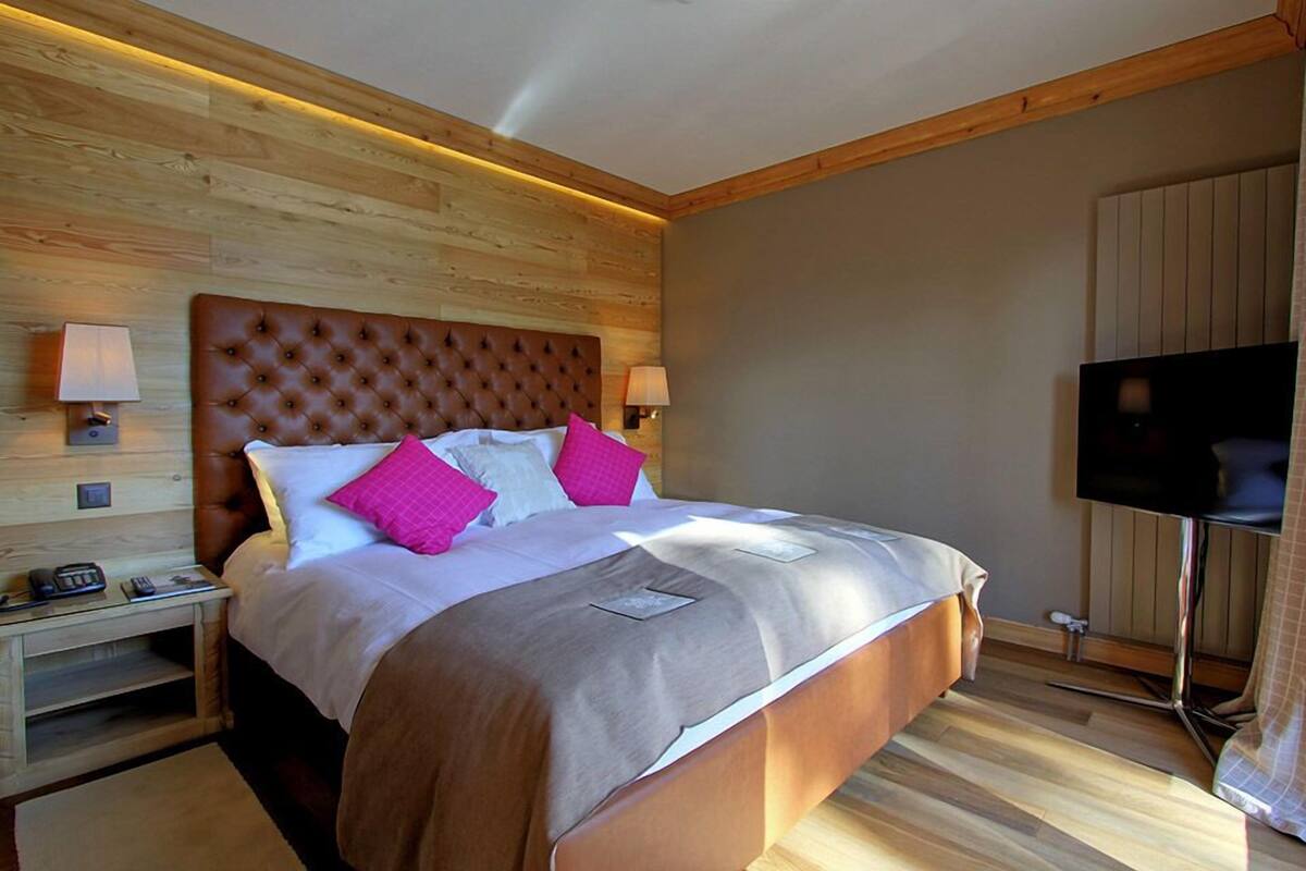 A bedroom with a large bed, wooden headboard, two bedside tables with lamps, and a flat-screen TV.