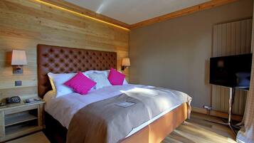 Un dormitorio con una cama grande, cabecera de madera, dos mesitas de noche con lámparas y un televisor de pantalla plana.