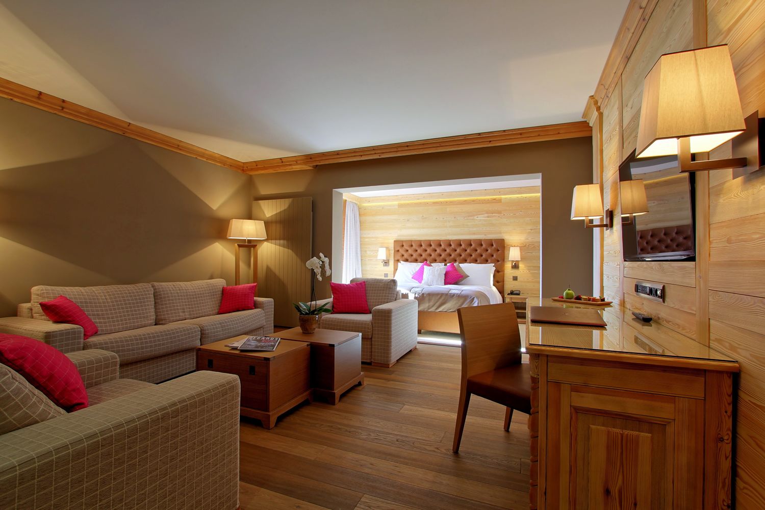 A hotel room with a large bed, a sofa, a chair, a small table, and a TV.