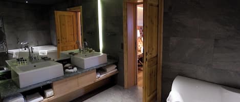 A modern bathroom with a large mirror, two sinks, a bathtub, and wooden cabinetry.