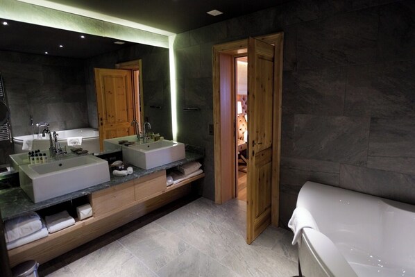 A modern bathroom with a large mirror, two sinks, a bathtub, and wooden cabinetry.