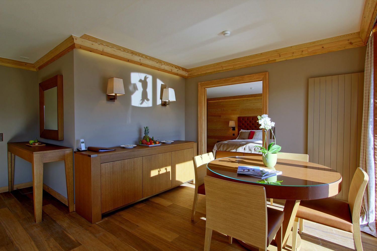 Une chambre d’hôtel avec un bureau en bois, un lit doté d’une tête de lit, une table à manger avec des chaises et un grand miroir au mur.