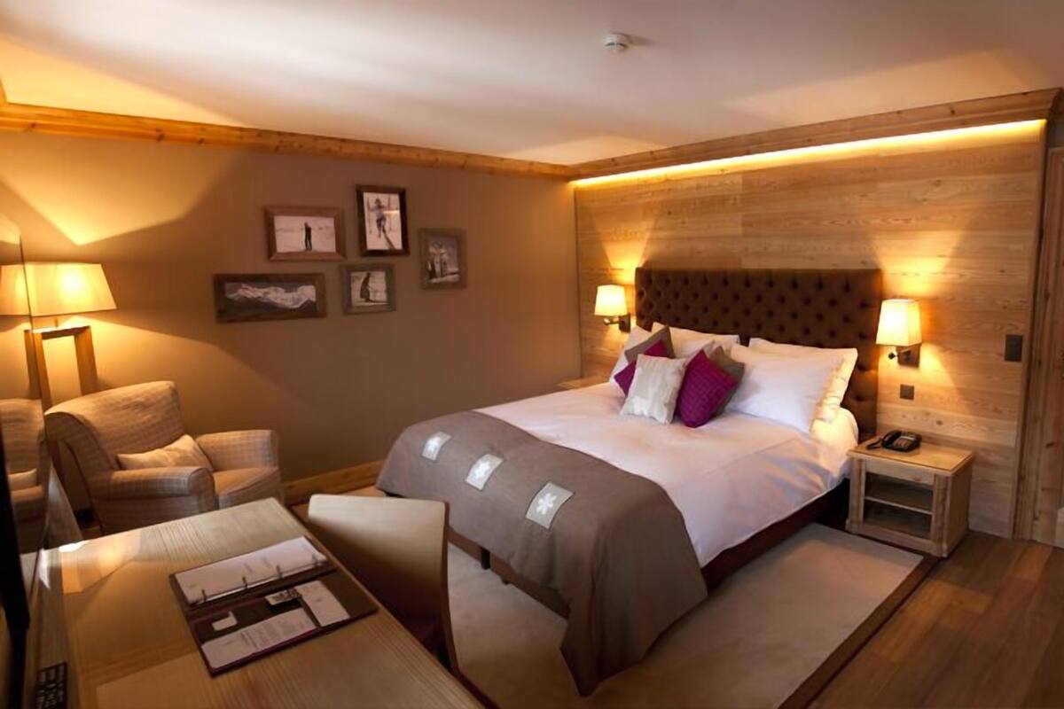 A cozy hotel room with a large bed, a wooden headboard, two bedside tables with lamps, a chair, and a desk with a lamp.