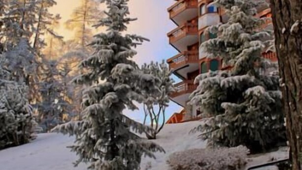 Un espacio exterior cubierto de nieve con un banco de madera, una escalera y un edificio con varios balcones.