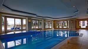 Una gran piscina interior con paredes de vidrio transparente, rodeada de suelo de baldosas y un techo alto.