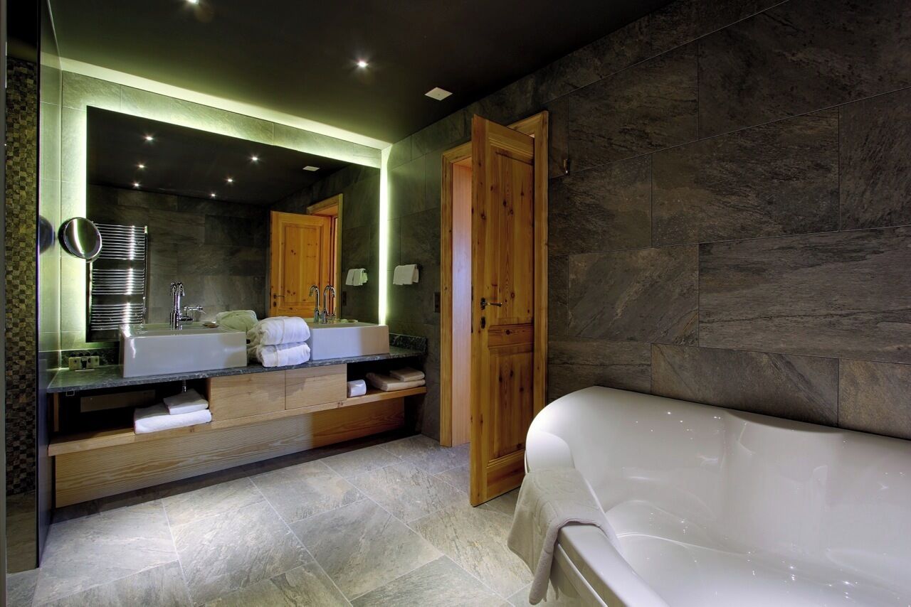 Ein modernes Badezimmer mit einem großen Spiegel, zwei Waschbecken, einer Badewanne und Holzschränken.