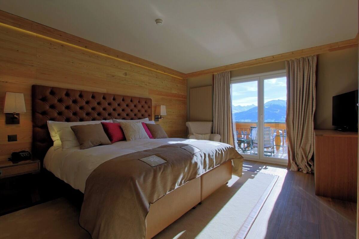 A spacious bedroom with a large bed, a television, and a balcony with a mountain view.