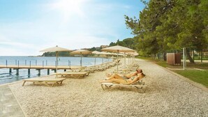 A beachside area with sun loungers and umbrellas, a pebble path, and a view of the sea. - Villas with Balcony or Terrace - Hotel & Resort Adria Ankaran (Ankaran)