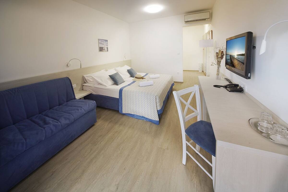 Um quarto com uma cama, um sofá azul, uma escrivaninha com uma cadeira e uma televisão.