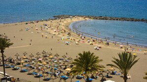 A beach with umbrellas, sun loungers, and people.