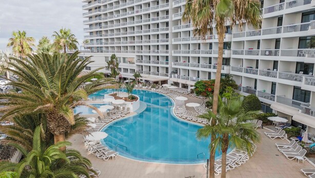 A hotel with a large pool surrounded by lounge chairs and palm trees.