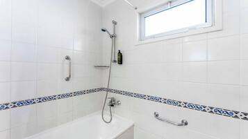 Un baño con paredes de azulejos blancos, una bañera, una ducha y un ventanal.