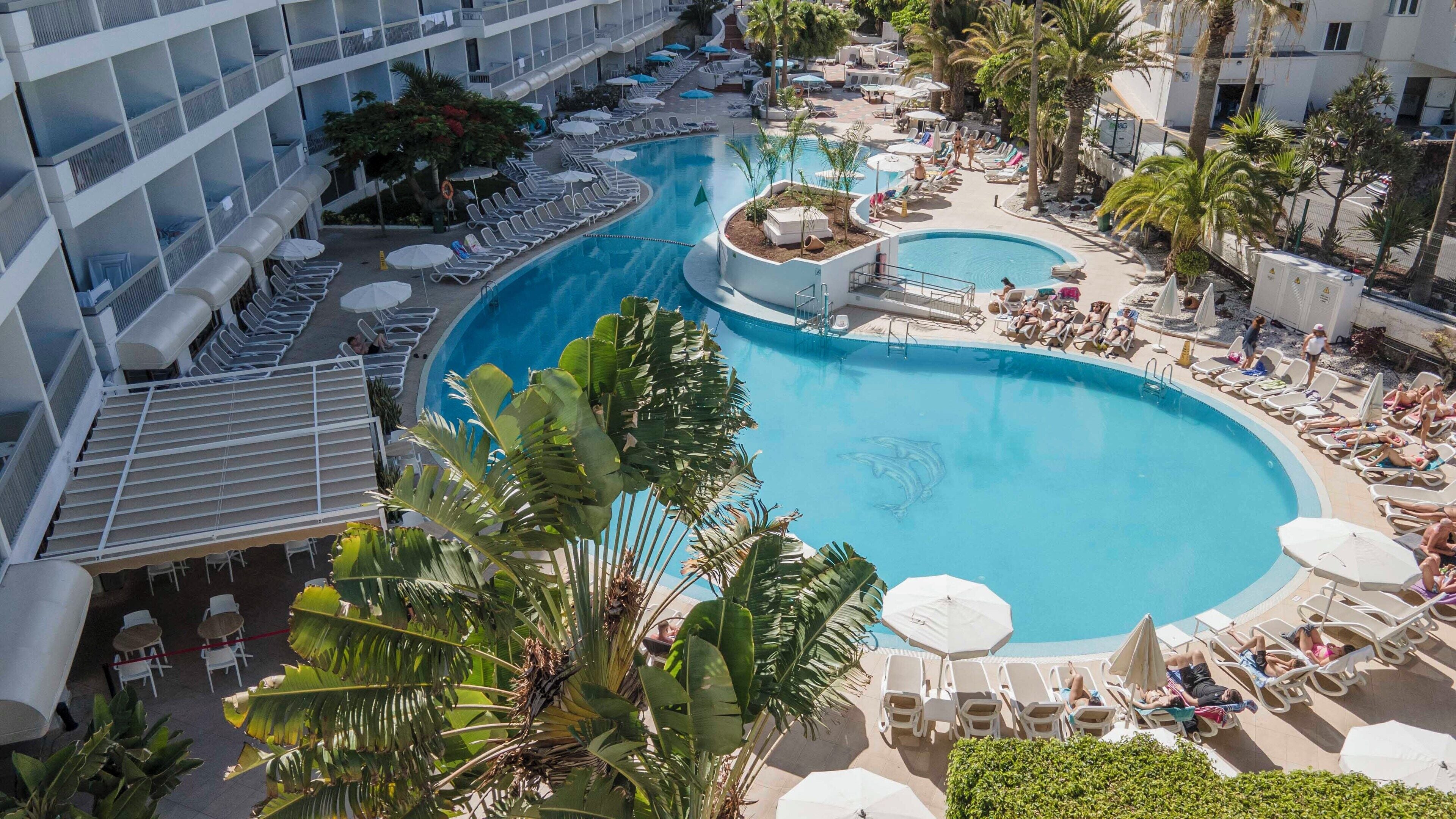 A resort pool area with multiple pools, sun loungers, and palm trees.