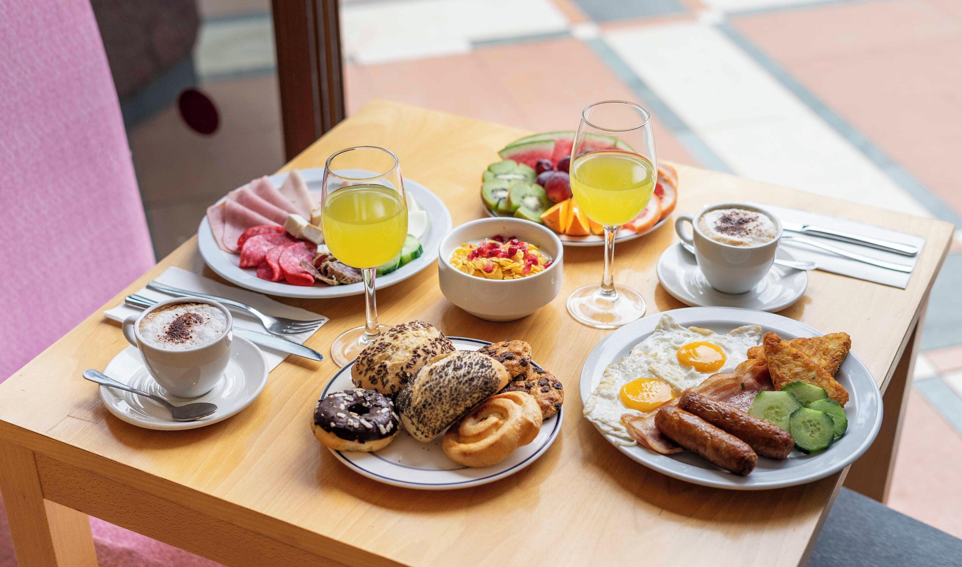 A breakfast table with plates of eggs, sausages, and pastries, accompanied by coffee and juice.
