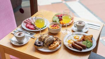 Et morgenbord med tallerkener med æg, pølser og bagværk, serveret med kaffe og juice.
