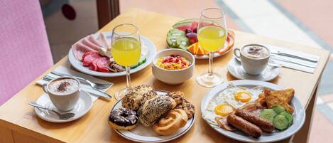 A breakfast table with plates of eggs, sausages, and pastries, accompanied by coffee and juice.