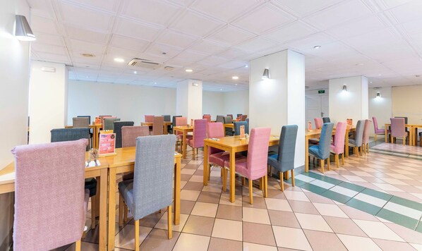 A spacious dining area with multiple tables and chairs, featuring a tiled floor and ceiling with recessed lighting.