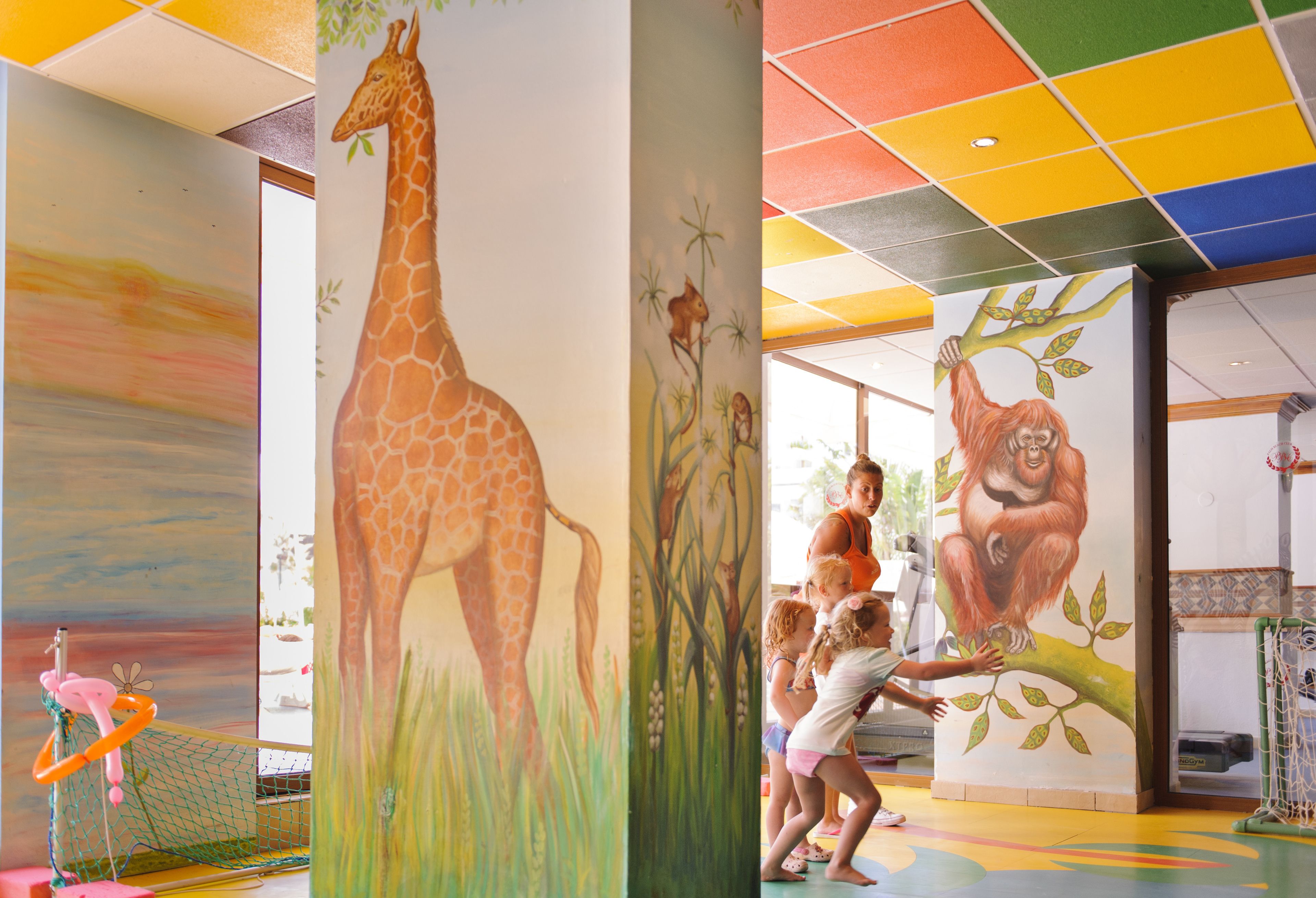 A colorful interior with murals of a giraffe and an orangutan, a netted play area, and a child interacting with the artwork.