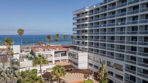 A high-rise hotel with multiple balconies overlooking a beach and the sea.