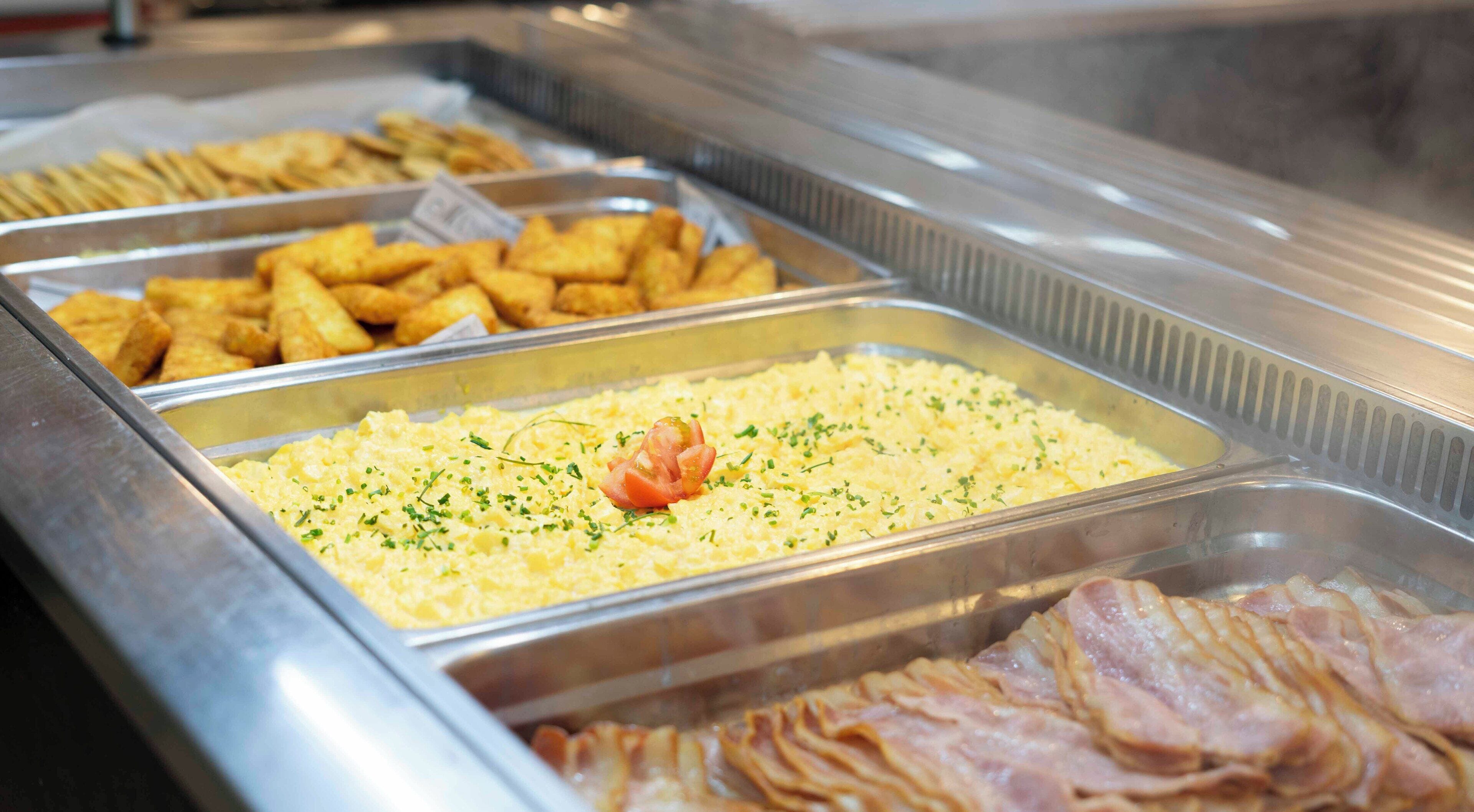 Ein Buffet mit verschiedenen Speisen, darunter Rührei, Speck und frittierte Speisen.