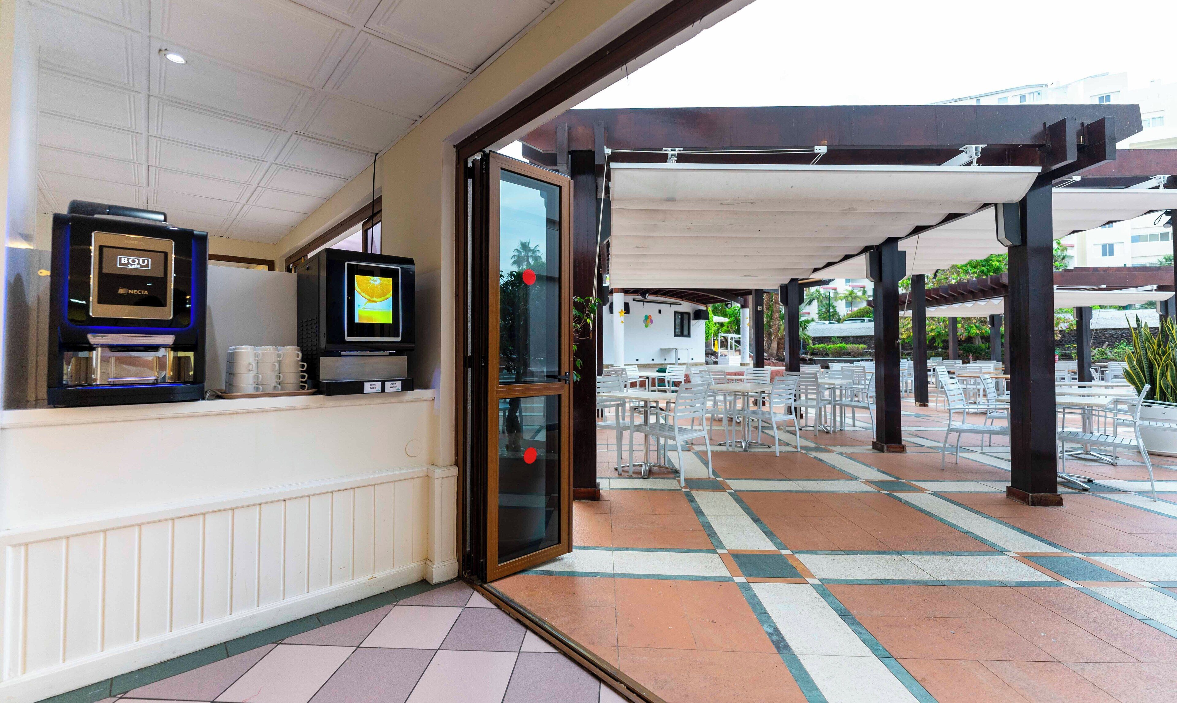 A hotel entrance with a reception area, a coffee machine, and a TV screen.