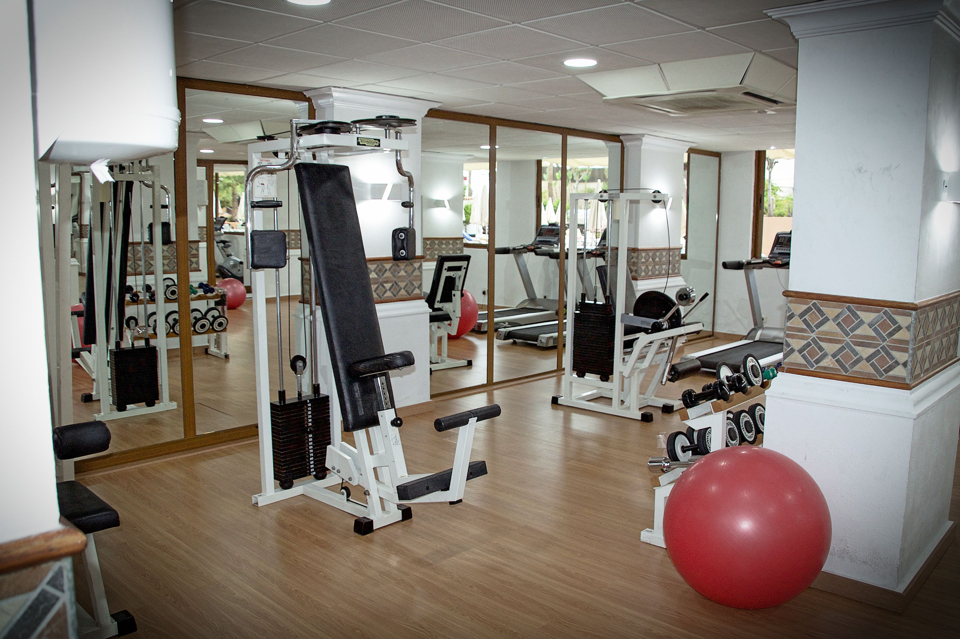 Un gimnasio con equipo de ejercicio, un espejo grande y una pelota roja para hacer ejercicio.