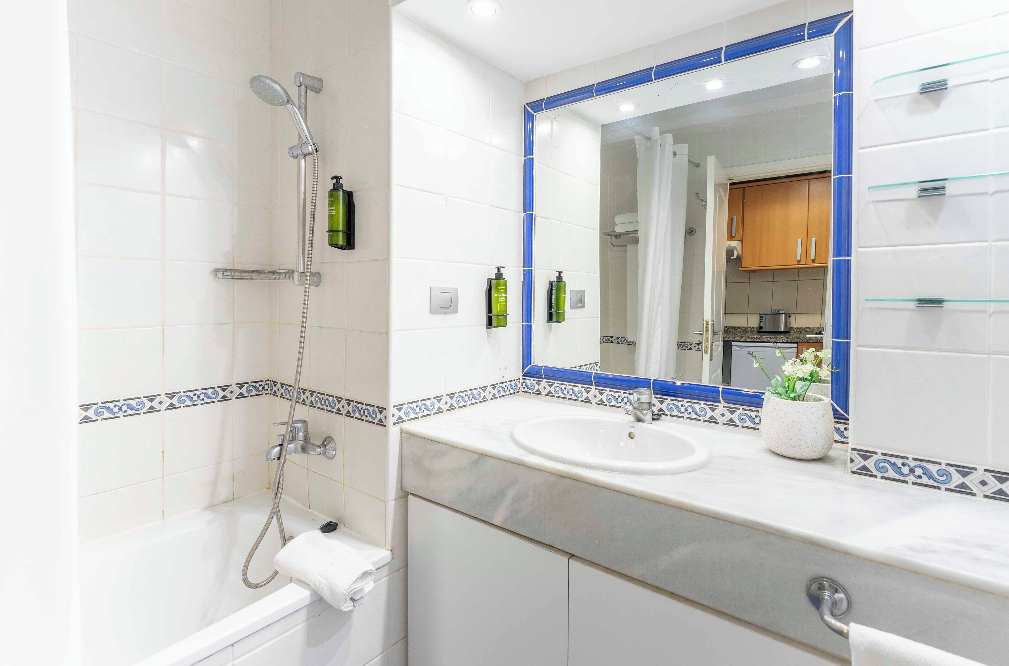 A bathroom with a bathtub, a sink, and a mirror. There are toiletries on the sink and a towel on the tub.