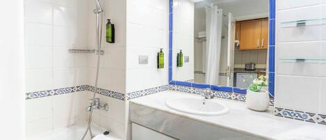 A bathroom with a bathtub, a sink, and a mirror. There are toiletries on the sink and a towel on the tub.