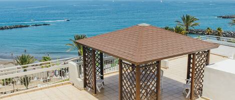 A covered outdoor seating area with a view of the sea and beach.