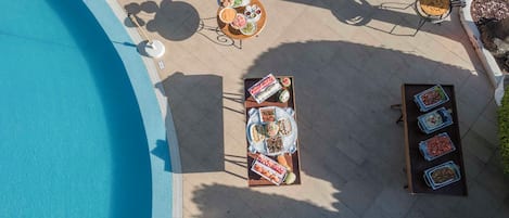 An outdoor dining area with a pool, tables, and a grill.