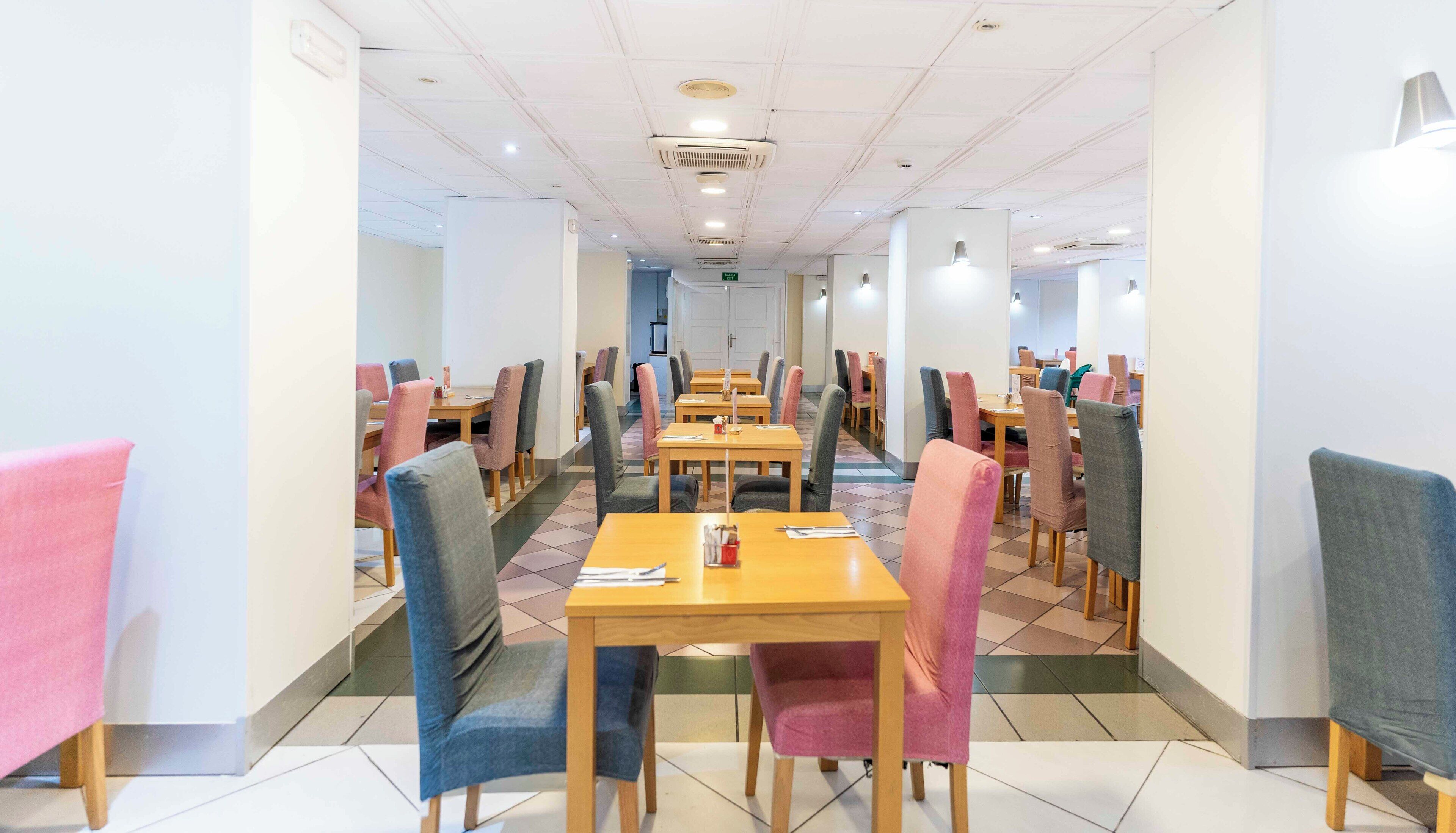A clean, modern dining area with multiple tables and chairs, featuring a neutral color palette and a tiled floor.