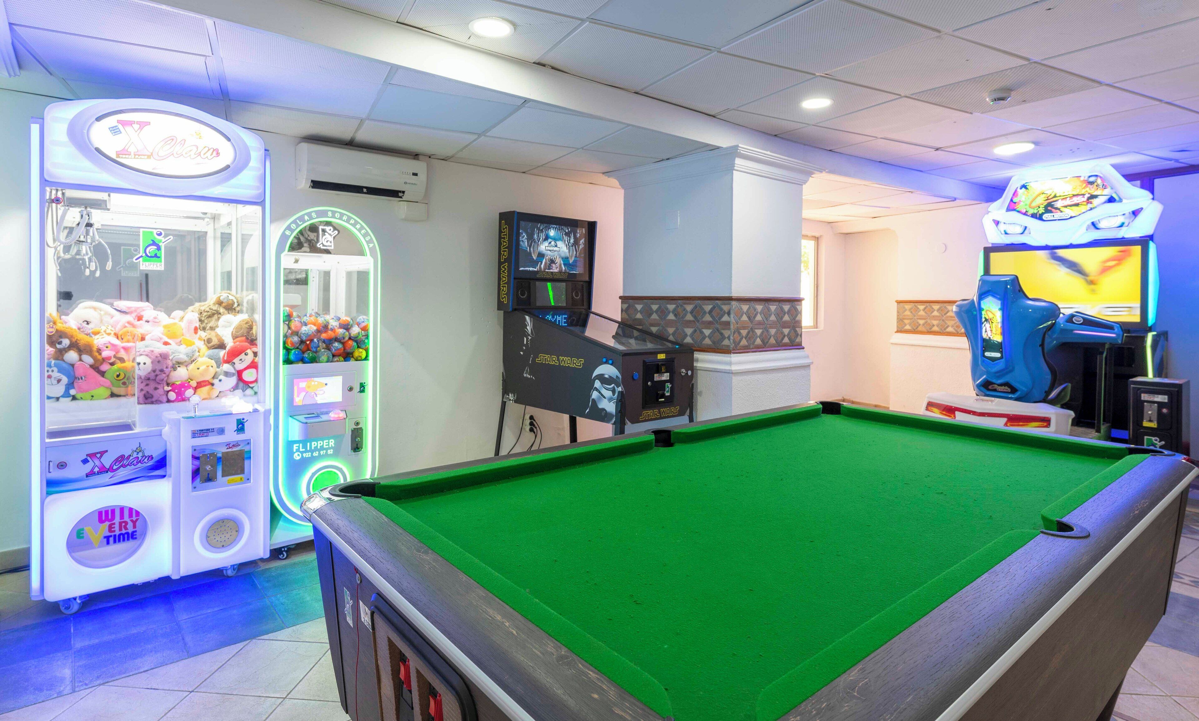 A pool table with a green felt surface, surrounded by claw machines and arcade games.