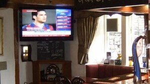 A bar area with a sign reading "SELECTION of Guest Beers" and a television displaying a news program. - The Kinder Lodge (High Peak)