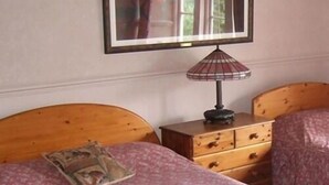 A bedroom with two wooden beds, a nightstand with a lamp, and a framed picture on the wall. - The Kinder Lodge (High Peak)