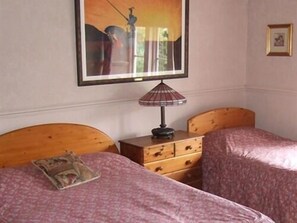 A bedroom with two beds, a wooden headboard, a nightstand with a lamp, a dresser, and a framed picture on the wall. - The Kinder Lodge (High Peak)