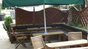 A wooden bench with a green canopy, wooden tables, and chairs in an outdoor seating area. - The Kinder Lodge (High Peak)