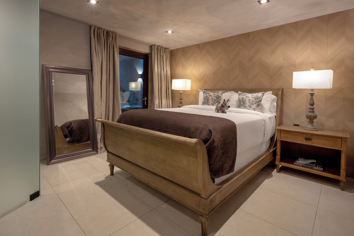 A hotel room with a large bed, two bedside tables with lamps, a mirror, and a wooden headboard.