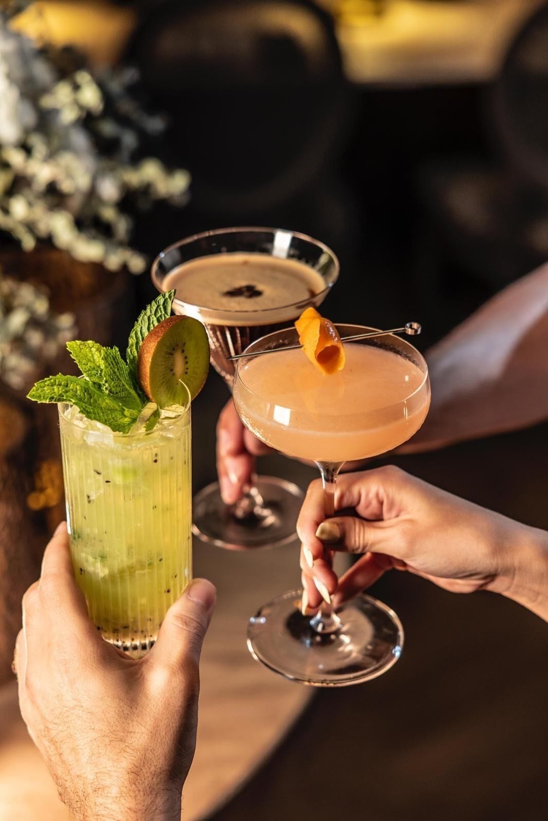 Two people holding cocktail glasses with garnishes.