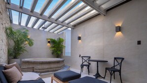 Uma área de estar moderna ao ar livre, com um banco de pedra, uma mesa de madeira e duas cadeiras.