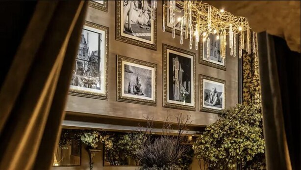 Restaurante com ambiente acolhedor, com obras de arte emolduradas nas paredes, uma mesa redonda central cercada por cadeiras e um candelabro.