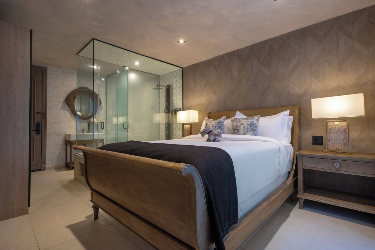 A modern bedroom with a wooden bed, a glass shower enclosure, and a nightstand with a lamp.