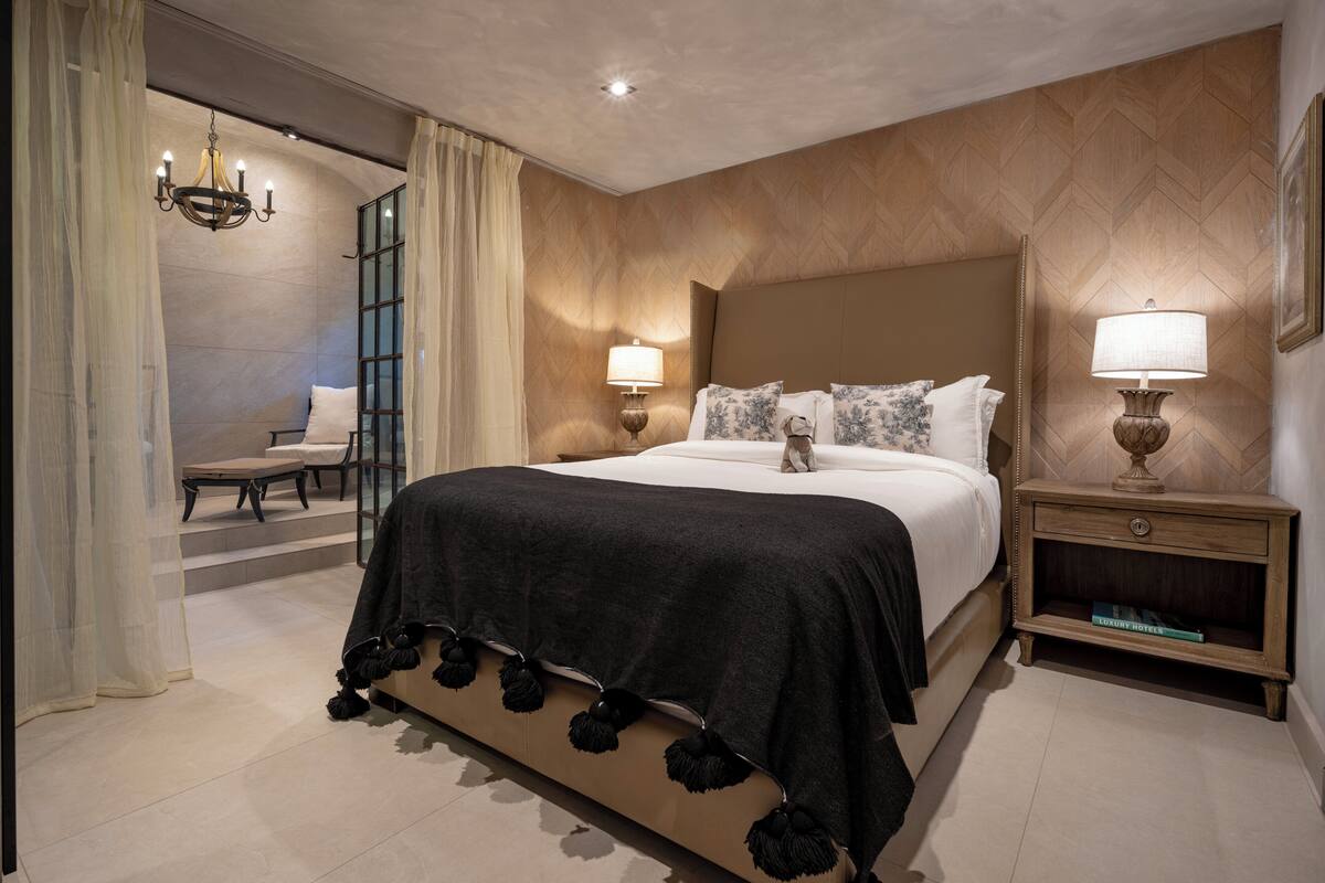 A hotel room with a large bed, two bedside lamps, a nightstand with a book, and a view of the hallway.