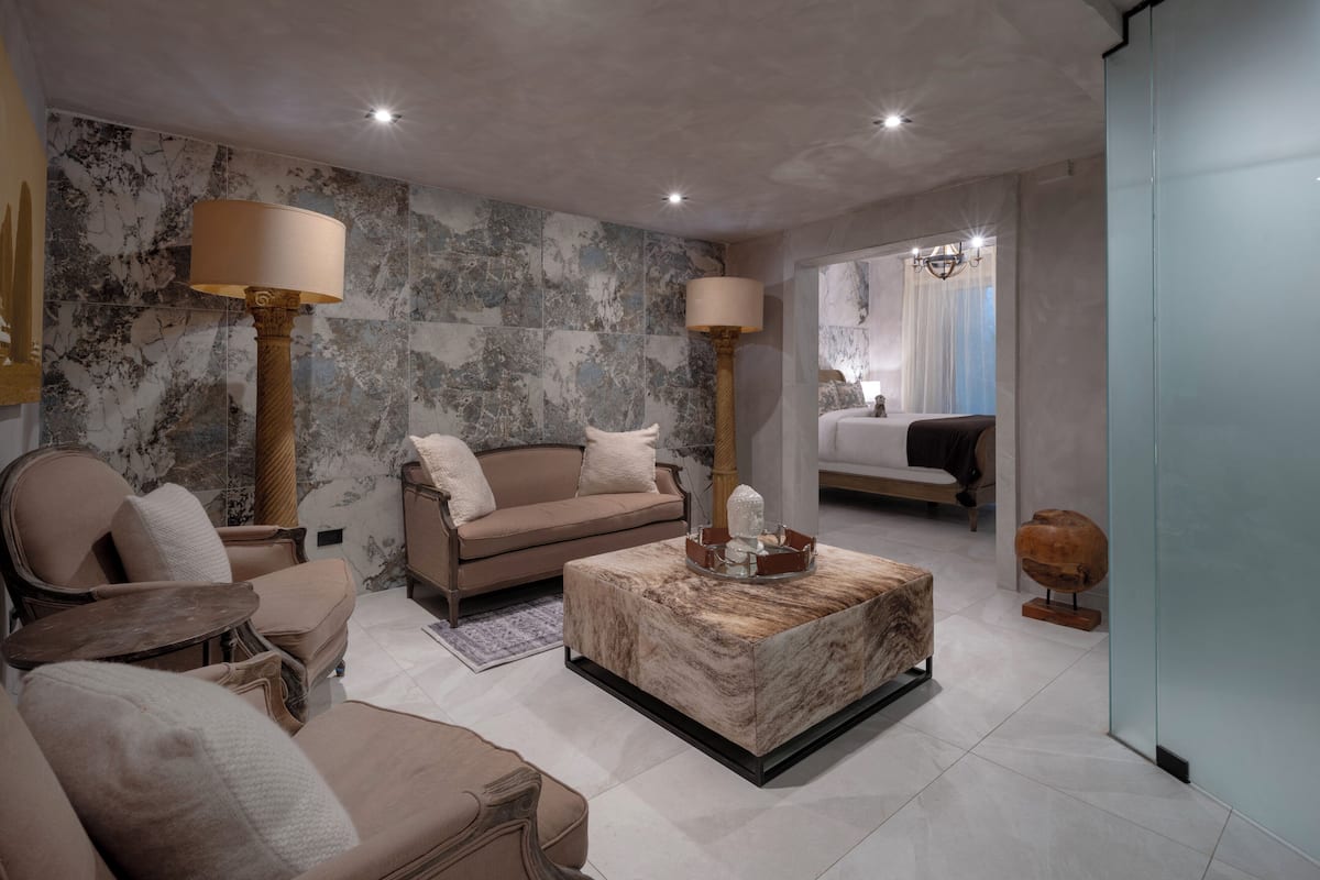 A modern living room with a marble wall, a sofa, a coffee table, and a bed in the background.