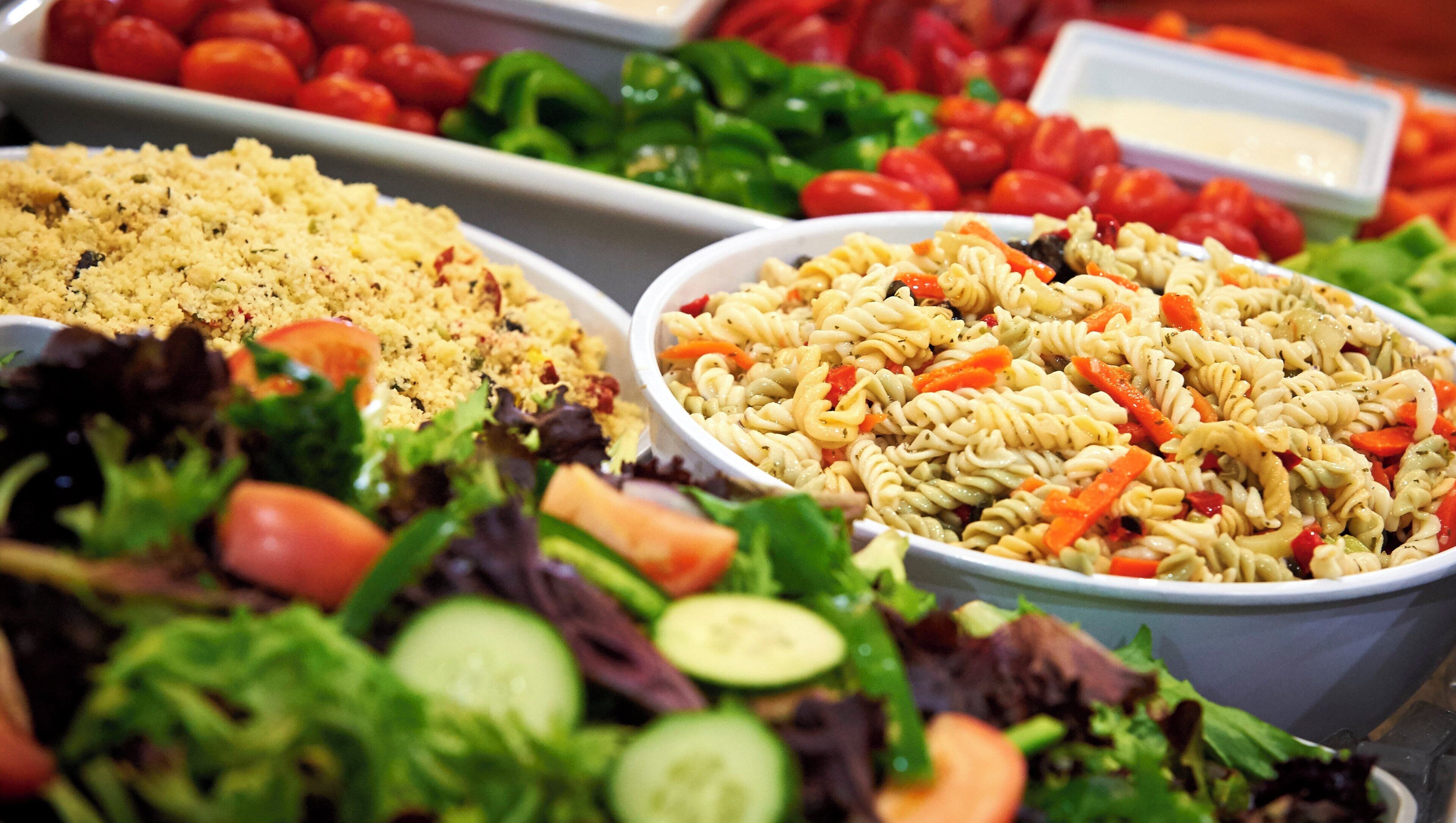 A buffet with various dishes including pasta salad, couscous, and a mixed greens salad.