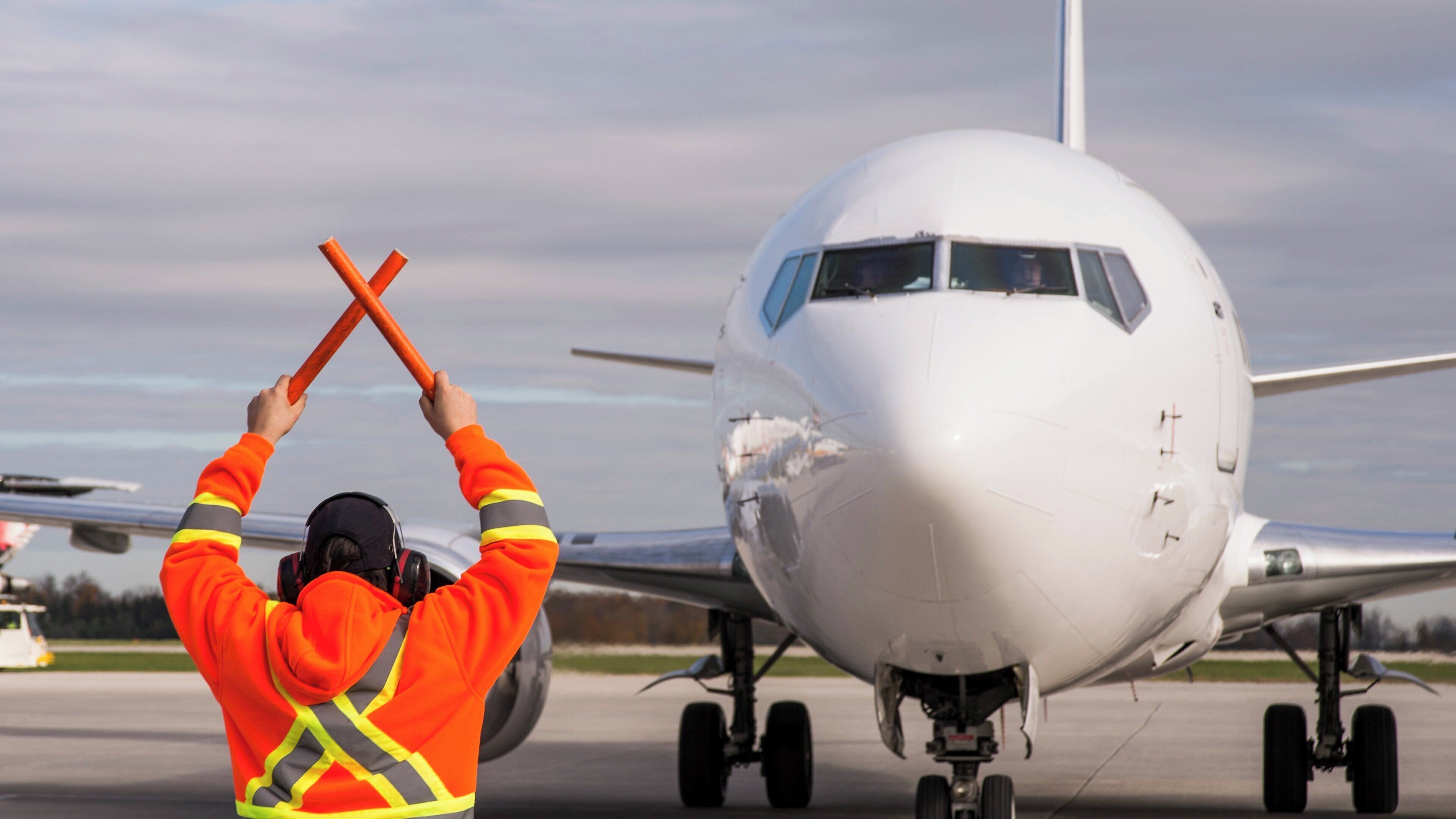A person in an orange safety jacket holding orange traffic cones in front of an airplane on a tarmac.