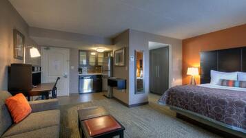 A hotel room with a bed, a sofa, a small table, a kitchenette, and a bathroom.