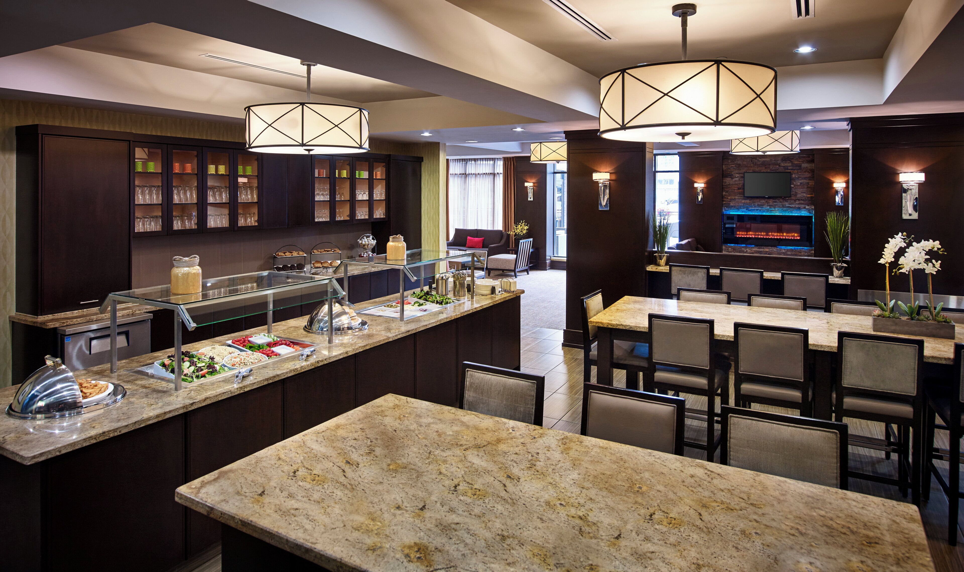 Un moderno vestíbulo de hotel con una barra central, zonas de estar y un mostrador de buffet.