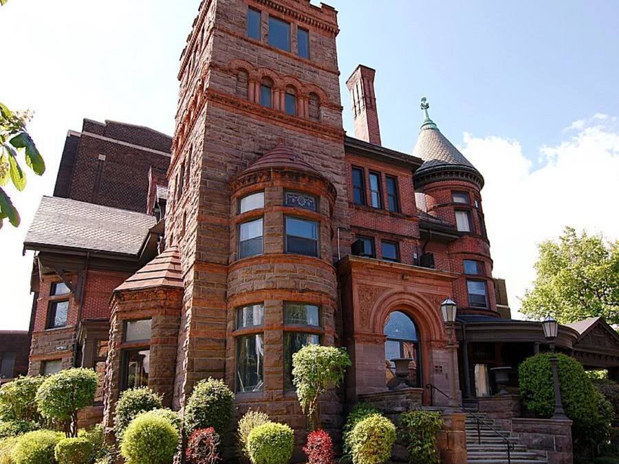A large, historic building with a prominent tower and turret, surrounded by well-maintained gardens.