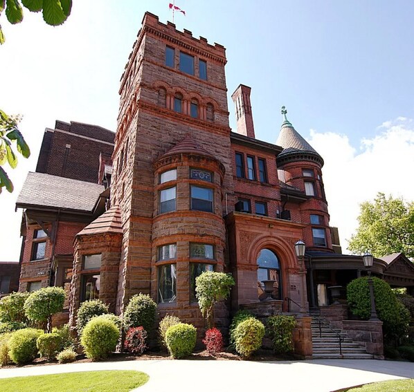 A large, historic building with a prominent tower and turret, surrounded by well-maintained gardens.